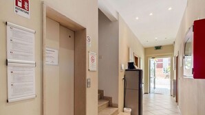 Un couloir d’hôtel avec un réfrigérateur, un panneau indiquant la sortie de secours et des panneaux d’information accrochés aux murs.