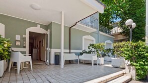 Un espace extérieur abrité, doté d’un sol carrelé, de mobilier en plastique blanc et de plantes en pot.