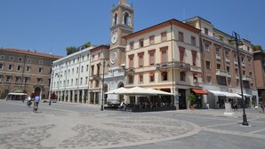Un bâtiment historique doté d’une tour horlogée, une cour intérieure avec des espaces de repos en plein air, et une rue où se croisent piétons et cyclistes.
