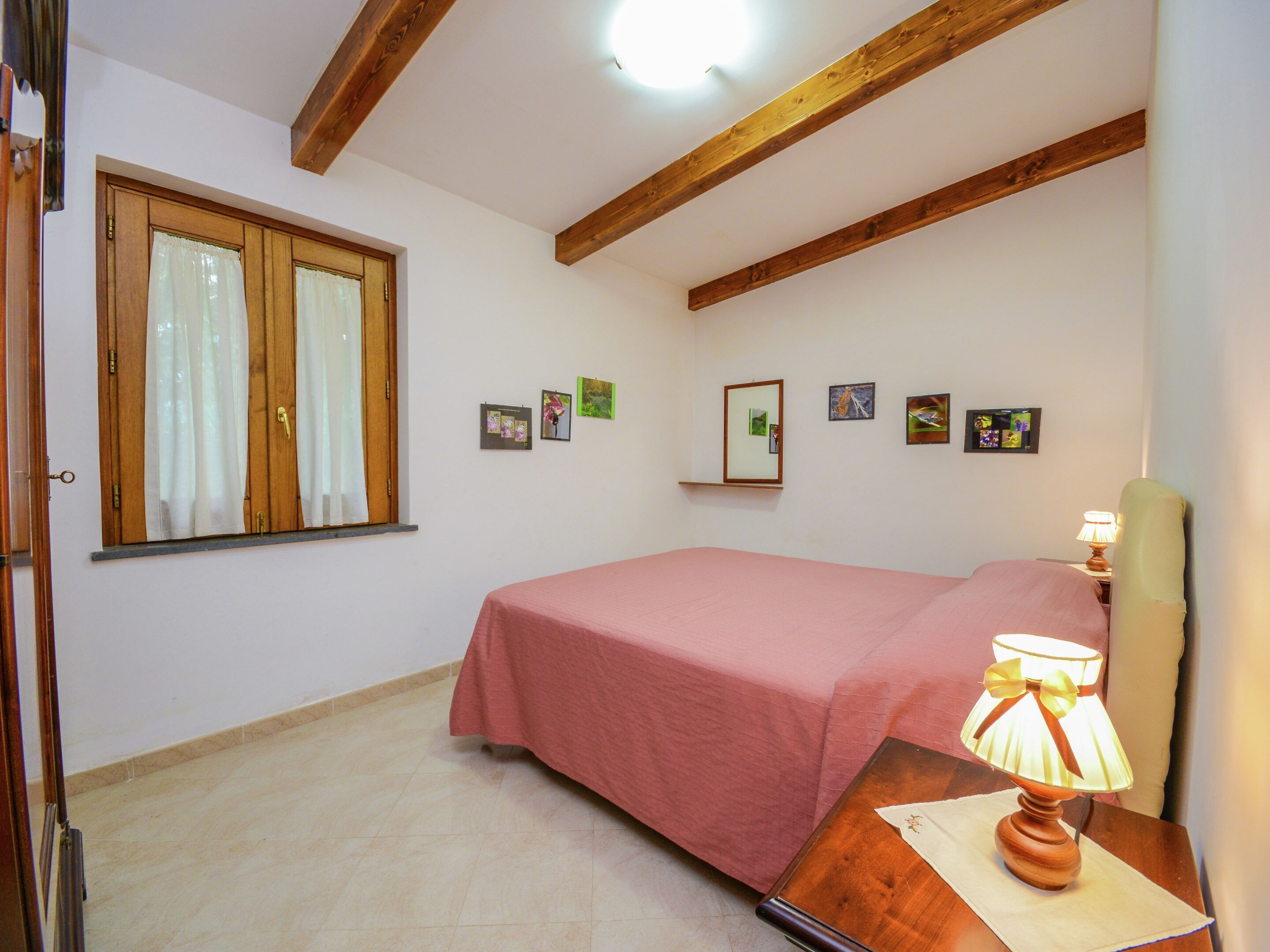 A bedroom with a single bed, a wooden headboard, a bedside table with a lamp, and a window with curtains.