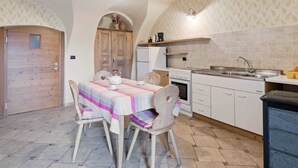 A kitchen with a dining area, featuring a wooden door, a table with a striped tablecloth, and a hanging light fixture.