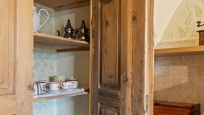 A wooden door leading to a kitchen with shelves holding various kitchenware and a tiled backsplash.