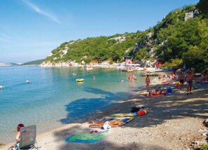 Ein Strand mit klarem Wasser, badenden Personen und Booten.