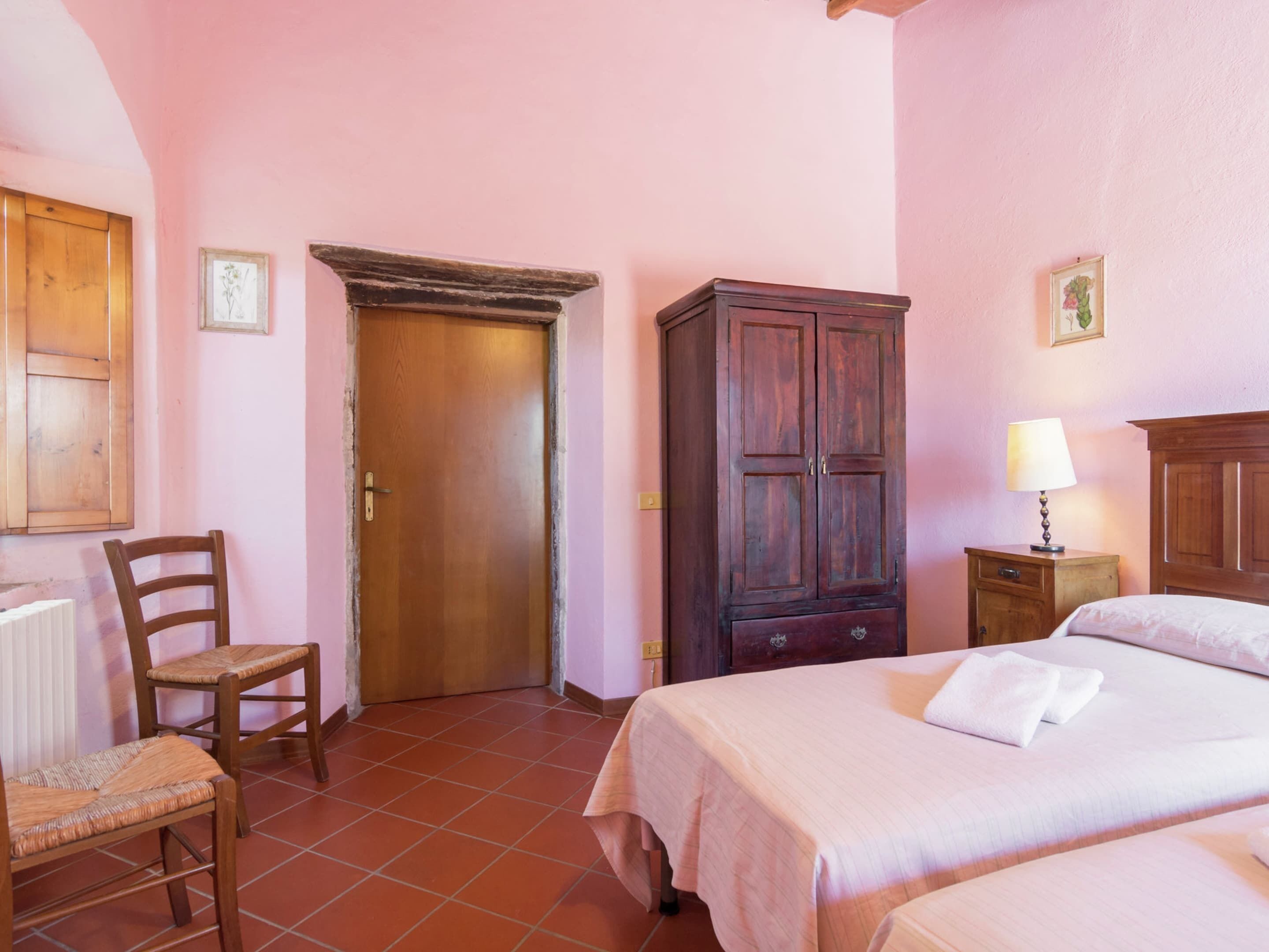 A bedroom with a bed, a wooden wardrobe, a chair, and a door.