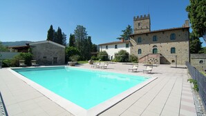 En swimmingpool med solstolar, en byggnad i sten med ett torn och en klarblå himmel.