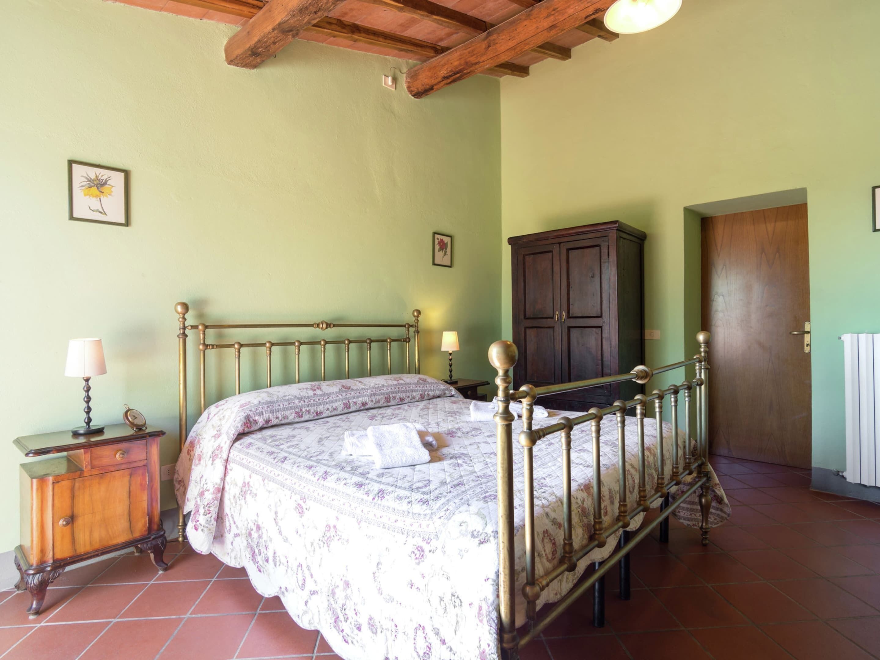 A bedroom with a bed, wooden wardrobe, and a nightstand with a lamp.