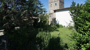 Ett historiskt stentorn med en vit byggnad i förgrunden, omgivet av frodig grönska.