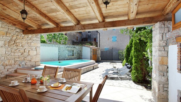 Ein überdachter Essbereich im Freien mit Pool, Steinmauern und Holzmöbeln.