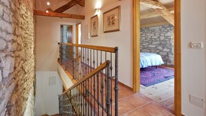 Eine Treppe mit Holzbalken und Metallgeländer, die zu einem Schlafzimmer mit Steinwand und Bett führt.