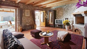 Ein rustikales Interieur mit Steinwänden, Holzbalken, einem Kamin, einem Fernseher und einem Sofa.