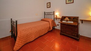 Una cama individual con colcha, un aparador de madera, una mesita de noche con lámpara y dos cuadros en la pared.