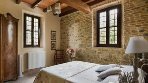 Ein rustikales Schlafzimmer mit Steinwänden, einem hölzernen Bett und einer Vintage-Lampe.