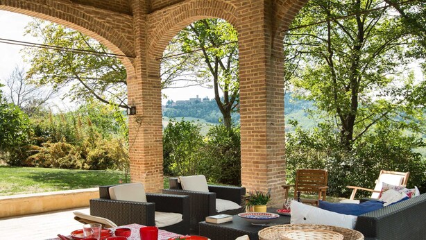 Eine Terrasse im Freien mit Korbmöbeln, einem Esstisch und einem schönen Blick auf die Hügel.