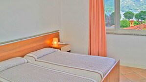 Un dormitorio con cama, una mesita de noche con lámpara y una ventana con vistas a la montaña y árboles.