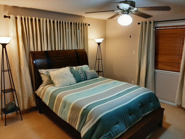 A bedroom with a bed, two standing lamps, a ceiling fan, and a window with blinds.