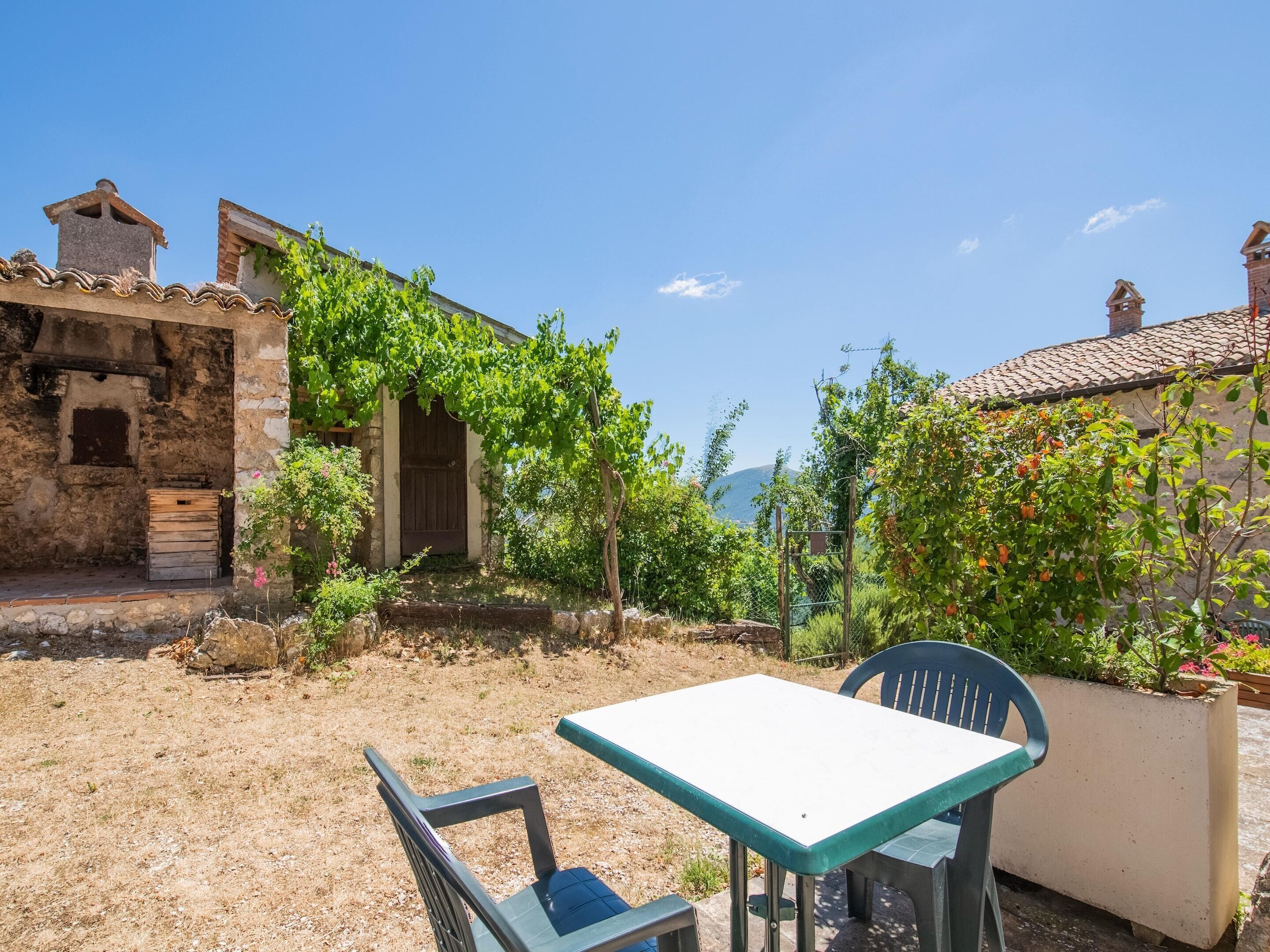 A rustic outdoor seating area with a table and chairs, surrounded by stone buildings and greenery.