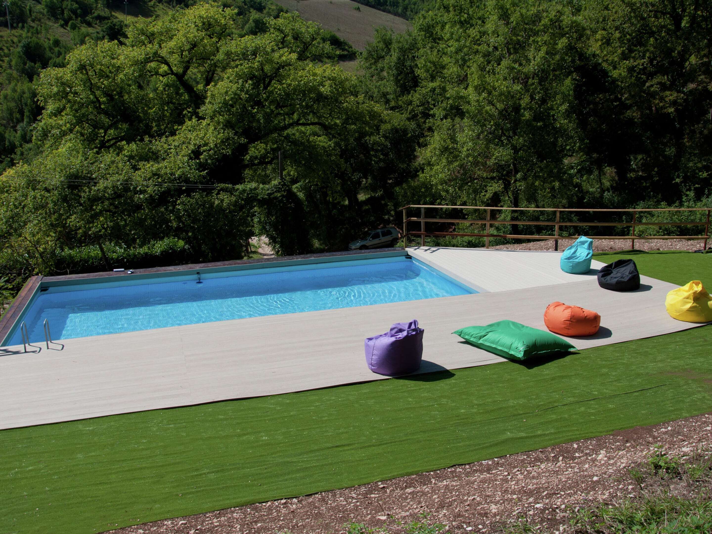 A swimming pool with a wooden deck and colorful bean bags.