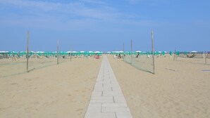 Un paseo marítimo bordeado de sombrillas y sillas de playa, que conduce al mar.