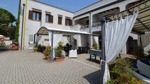 Un patio con zona de estar cubierta, mobiliario exterior y plantas en macetas.
