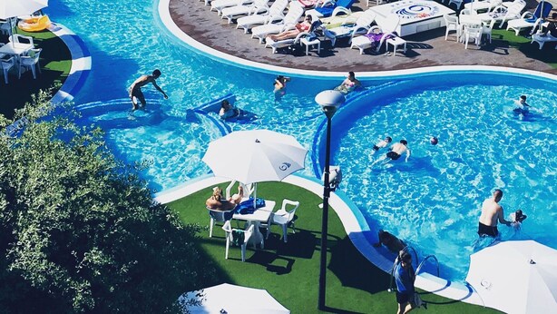 Una gran piscina exterior con varias pistas, rodeada de tumbonas y sombrillas.