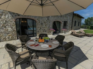 A stone building with a patio table set for dining, surrounded by wicker chairs. - Scenic Stay in Poppi With Pool (Poppi)