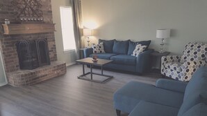 A living room with a fireplace, a sofa, a coffee table, and a patterned armchair.
