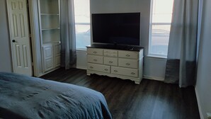A bedroom with a bed, a dresser, a television, and a window with curtains.