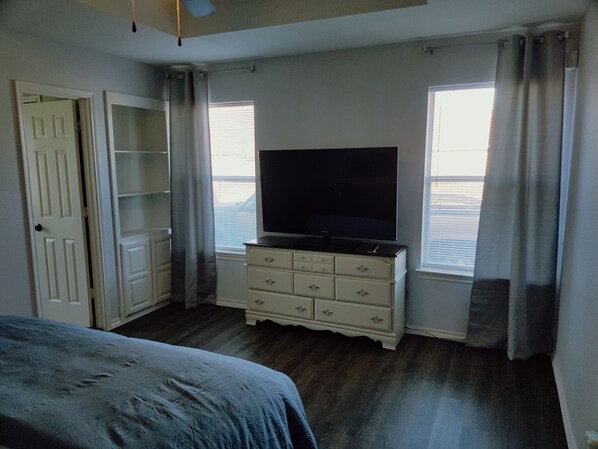 A bedroom with a bed, a dresser, a television, and a window with curtains.