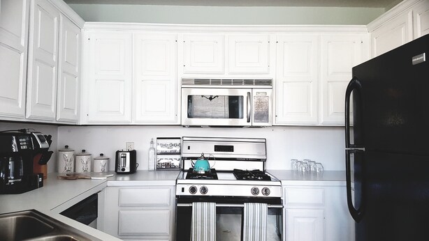 A kitchen with white cabinets, a black refrigerator, a stove, a microwave, and a sink.