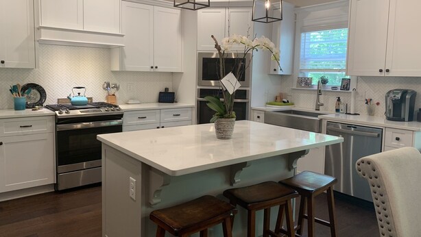 Una cocina moderna con armarios blancos, electrodomésticos de acero inoxidable, una isla central con taburetes e iluminación colgante.