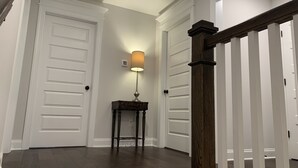 Un pasillo con puertas blancas, piso de madera y una lámpara sobre una mesita.