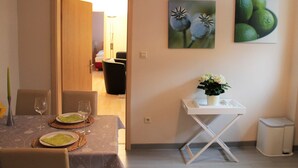A dining area with a table set for two, a small white side table with a vase, and two framed pictures on the wall. - Ferienwohnung, Nienhagen (Nienhagen)