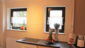 A kitchen with a stove, oven, sink, and windows with lace curtains. - Ferienwohnung, Nienhagen (Nienhagen)