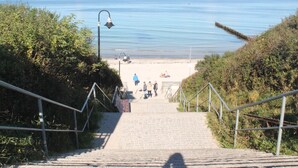 A staircase leading to a beach with a clear view of the sea and a distant ship. - Ferienwohnung, Nienhagen (Nienhagen)