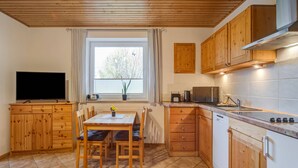 A compact kitchen with wooden cabinets, a dining table with chairs, a TV, and a window with curtains. - Idyllic Apartment in Kühlungsborn Germany near Forest (Kuehlungsborn)
