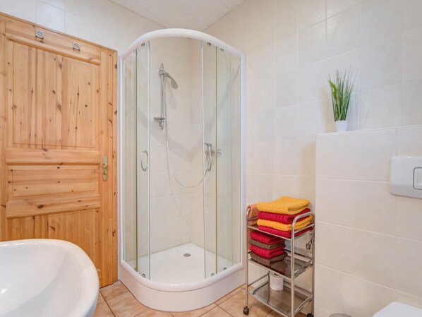 Un baño con ducha envuelta en vidrio, puerta de madera, bañera blanca y toallero metálico con toallas dobladas.
