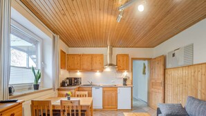 A compact kitchen with wooden cabinets, a dining area with a table and chairs, a small refrigerator, and a sofa in a living area. - Idyllic Apartment in Kühlungsborn Germany near Forest (Kuehlungsborn)