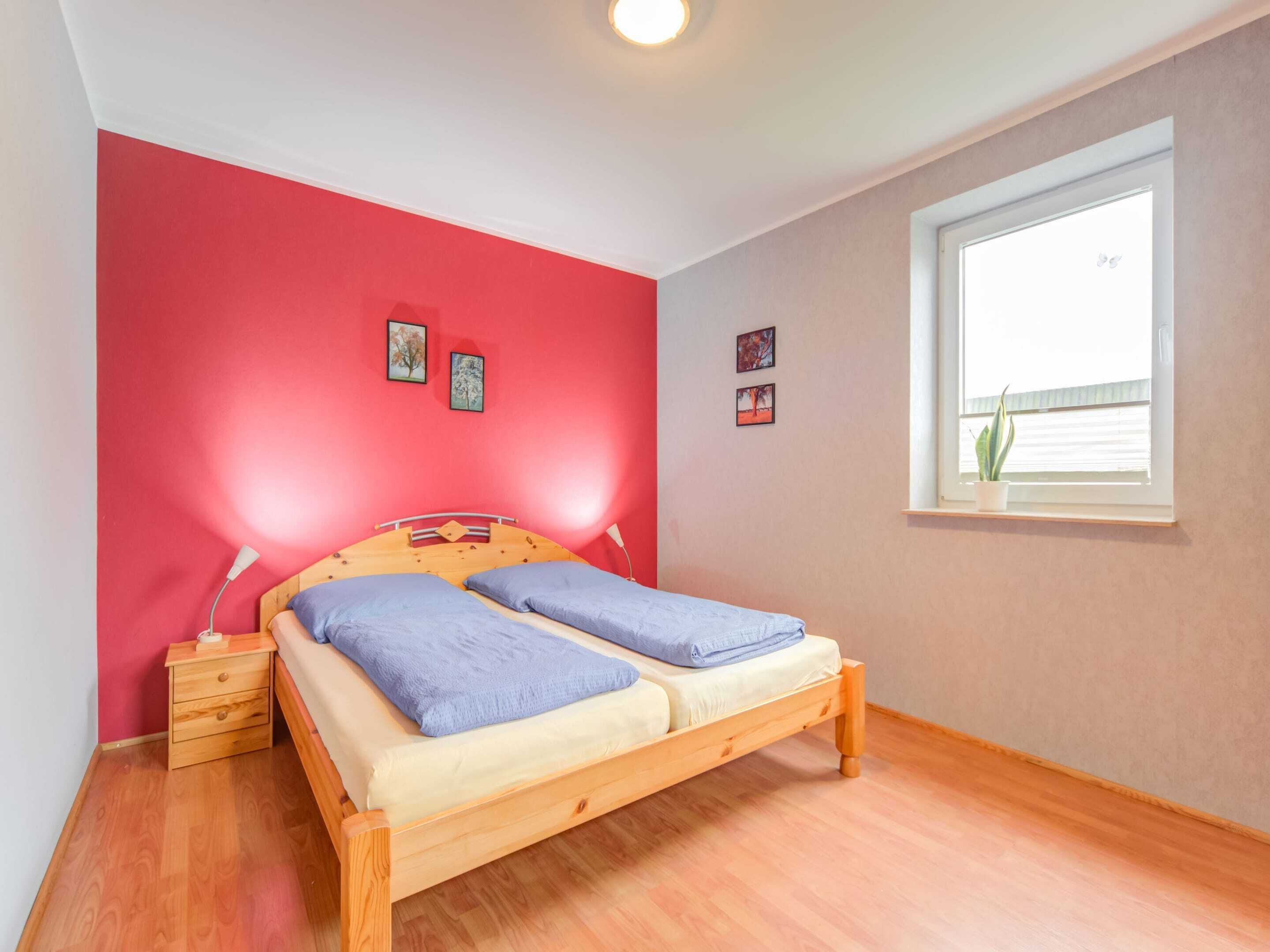Une chambre à coucher avec un lit en bois, une table de chevet, une fenêtre avec une plante et deux tableaux accrochés au mur.