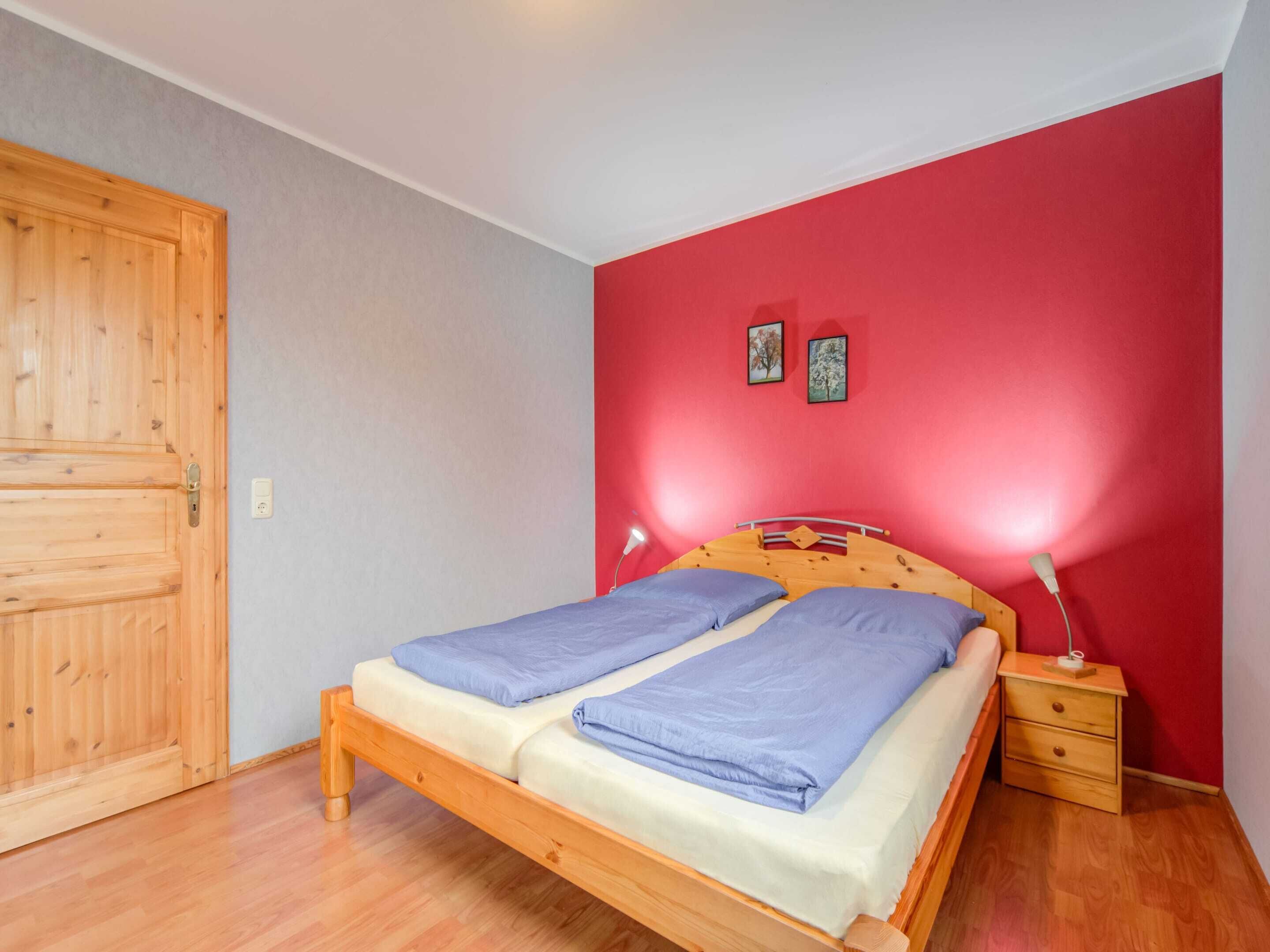 Een slaapkamer met een houten bed, twee nachtkastjes, een rode wand en een houten deur.