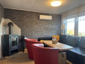 A cozy living area with a stone wall, a wood-burning stove, red leather chairs, and a wooden table. - Holiday Home in Sternberg by Lake (Sternberg)