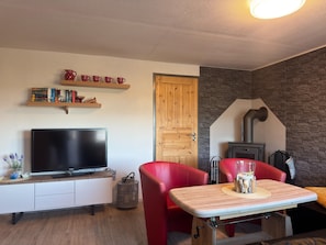 Un salon chaleureux avec un téléviseur à écran plat, un fauteuil rouge, une table en bois et un mur en pierre.