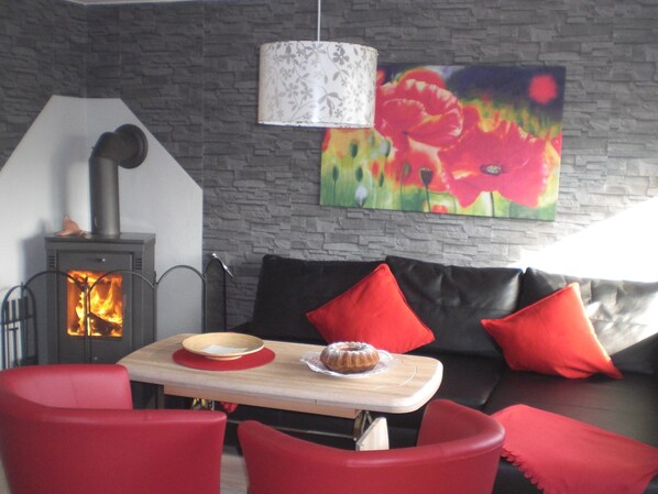 A cozy living room with a fireplace, a sofa with red cushions, and a table with a bowl and a cake.