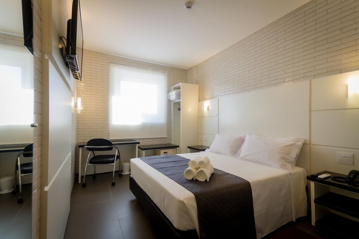 A hotel room with a bed, a desk, a chair, and a window.