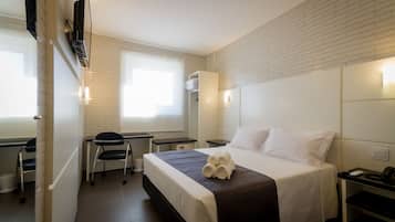 A hotel room with a bed, a desk, a chair, and a window.