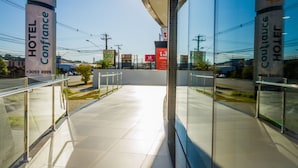 Una entrada de hotel moderna con puertas de vidrio, señalización clara para HOTEL Confidence y COUTEAUQUES HOTEL, y un pavimento de baldosas limpias.