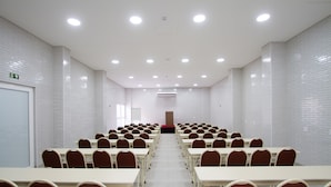 Un salón de conferencias con paredes de azulejos blancos, varias mesas y sillas rojas dispuestas en filas.
