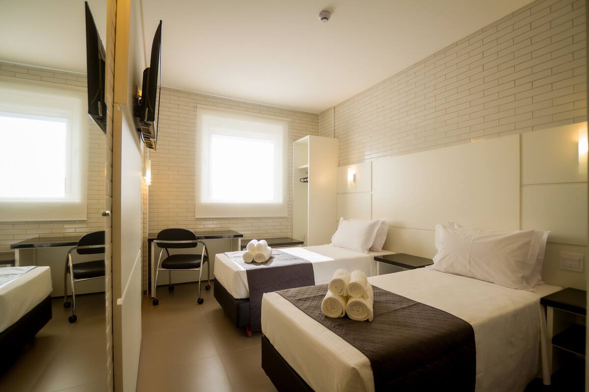 A hotel room with two beds, a desk, a chair, and a TV.