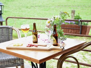 A wooden table with a bottle of beer, a glass, and a cutting board with meat.