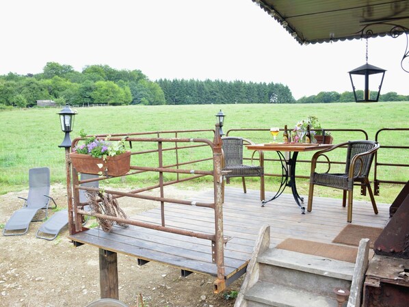 A rustic outdoor seating area with a wooden deck, metal railing, and wicker chairs.