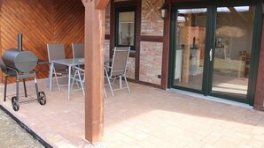 An outdoor patio with a grill, chairs, and a sliding glass door leading to a backyard. - Farmhouse Near Baltic Sea Kuhlungsborn (Kroepelin)